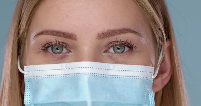Close up and crop frame of young woman posing in medical face mask. Looking at camera with smile
