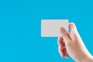 Close up of a female hand holding a blank white business card on a blue background. Business idea, copy space