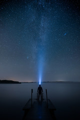 A man with flashlight standing on a pier by a lake and looking at the stars