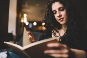 Fototapeta premium Thoughtful young lady reading interesting book in cozy armchair