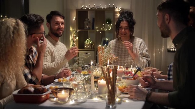 holidays, food and people concept - happy smiling friends having christmas dinner, eating and talking at home in evening
