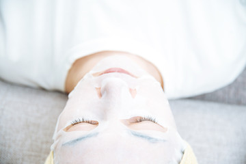 Obraz na płótnie Canvas Young woman resting with a white textile facial moisturizing mask.