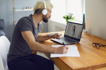 University college online education. A guy student in headphones teaches a lecture online with a teacher video call with a laptop while sitting at home.