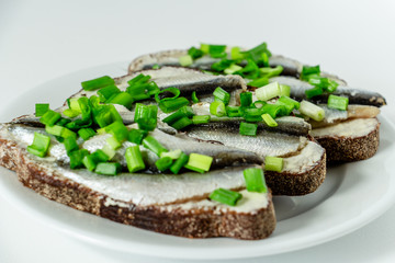 three delicious sandwiches with rye bread, butter, small sardines and green onions on a white plate on a white background
