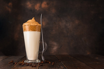 A long glass with very trendy whipped Dalgona coffee against dark background