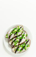 three delicious sandwiches with rye bread, butter, small sardines and green onions on a white plate on a white background, white space