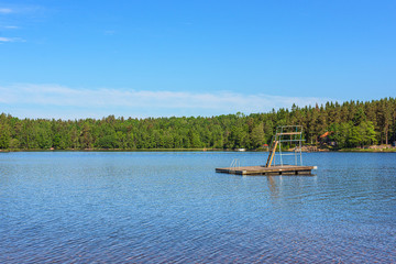 A float in a lake with a diving tower. Forests in the background.