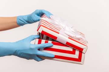 Profile side view closeup of human hand in blue surgical gloves holding and opening red white striped gift box. indoor, studio shot, isolated on gray background.