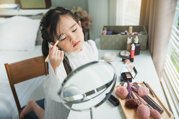 Child cosmetics Cute little girl with lipstick and mirror in bedroom. Happy child. Little pretty...