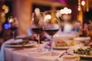 Banquet. Cover the table with a white tablecloth. On the table are glasses of wine, dishes with food. Against bokeh