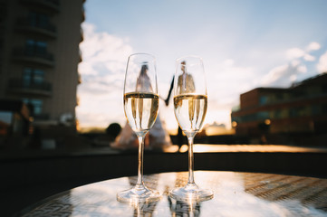 Two glasses of champagne stand on a table stand on a table. A loving couple of newlyweds is standing in the background. 