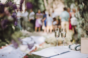 Two glasses of champagne stand on a table stand on a table. Nearby lies a pillow with wedding rings. Amid a lot of people