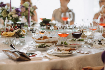 Banquet. Cover the table with a white tablecloth. On the table are glasses of wine, dishes with food. Amid a lot of people