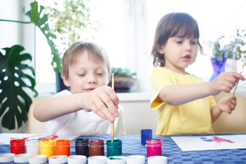 Children engaged in creativity in the home interior. Child draws and colors picture with paints and brush. Developing activities and leisure during self-isolation and quarantine. Foreground focus