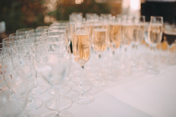 Many glasses with champagne are on the table. The table is covered with a white tablecloth