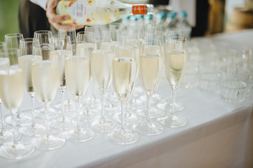 Many glasses with champagne are on the table. The table is covered with a white tablecloth