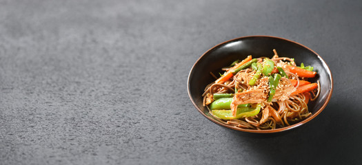 A bowl of wok noodles stands on a black table background with a copy space