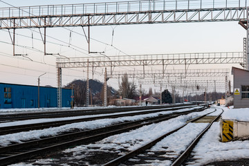 A railway station with long rusty metal iron rails and wooden sleepers among rocks and melting snow