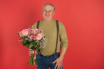 An elderly man with a large beautiful bouquet of flowers stands on a red background, the concept of a holiday and a happy old age