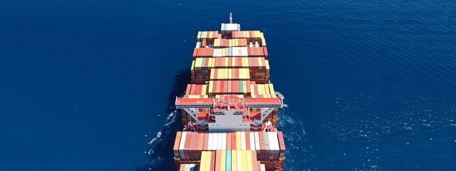 Fototapeta premium Aerial ultra wide photo of Container cargo Ship carrying load in truck-size colourful containers in deep blue open ocean sea 