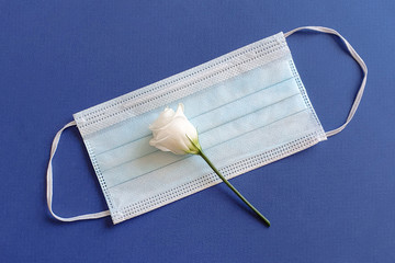 White flower lies on a medical mask. Blue background. Concept of protection. Memory of the victims...