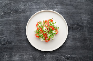 Caprese is a traditional Italian vegetable salad with mozzarella cheese, cherry tomatoes and arugula microgreens. Top view with copy space. Dark wooden rustic background.