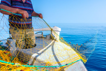 Fisherman is fishing fresh fishes using yellow fishing nets, on fishing boat, Crete, Greece.