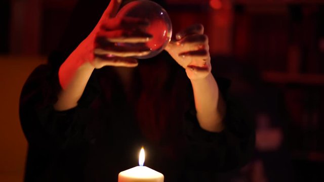 Girl in black robe guesses on crystal ball in light of candle flame