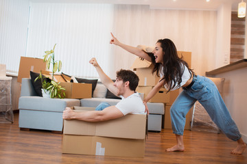 Happy couple is having fun with cardboard boxes in new house at moving day