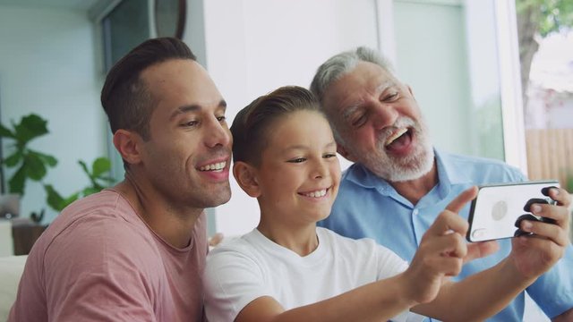 Multi-generation male hispanic family at home on sofa posing for selfie on mobile phone - shot in slow motion