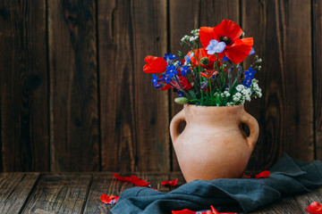 Wildflowers in a clay vase on a wooden table, a bouquet of poppies, still life