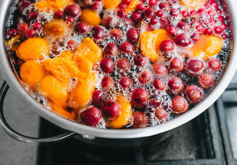 Fresh fruits are boiled in boiling water in a metal pan on the stove. Delicious stewed apricot, apples, cherries, raspberries. Photography, concept.