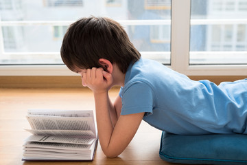 Nine years old child reading book lying on pillow. Soft focus. Quarantine and online school concept