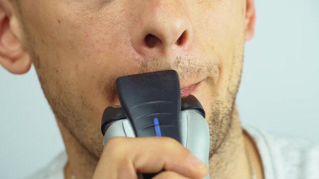 young man shaving with an electric razor. The guy shaves his beard with a razor close-up macro.