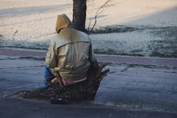 Lonely unknown person sitting on the stump and read book. Man in old dirty clothes. Pandemic coronavirus isolation concept photo. View from the back. - Powered by Adobe