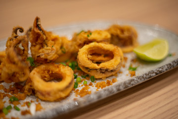 Fried squid rings with lemon on wooden table as appetizer seafood background.