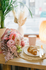 Cappuccino and almond croissant on a plate. Bouquet of beautiful flowers. Flat lay. Coffee shop concept.