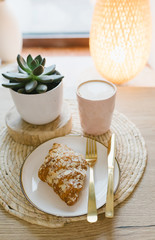 Almond croissant on a plate, cappuccino and succulent. Concept of cafe and pastry shop. Stylish breakfast.