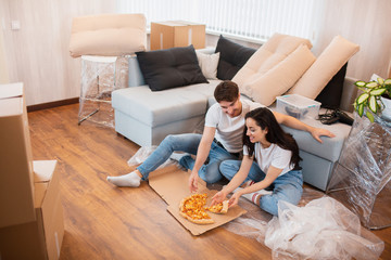 Happy family eating pizza on moving day. Picture of a young couple enjoying rest time while sitting together in the new house.