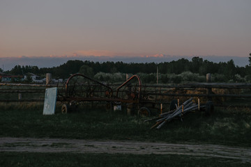 Fototapeta na wymiar Evening landscape in the village. Panoramic view of the tractor mower lying on the wooden poles. | KOROVYAKOVA, SVERDLOVSKAYA OBLAST - 9 MAY 2020.