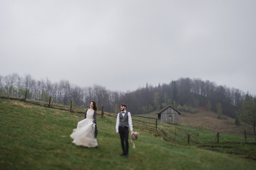 Fototapeta premium Romantic, young and happy caucasian couple in wedding clothes hugging on the background of beautiful mountains. Love, relationships, romance, happiness concept. Bride and groom traveling together.