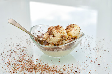 Bowl with delicious vanilla ice cream sprinkled with chocolate chips with a spoon on the table on a light background