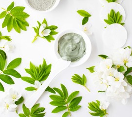 SPA facial clay masks in bowls and tropical leaf on white background. Flat lay, top view. Natural organic beauty products, face skin care 