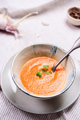 Healthy Vegetable Cream Soup in a bowl served with microgreen on white striped linen tablecloth. Vertical composition. Selective focus