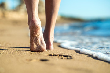 Close up of woman feet walking barefoot on sand leaving footprints on golden beach. Vacation, travel and freedom concept. People relaxing in summer.