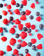 Flying berries on a blue background. Falling raspberry and blueberries fruits