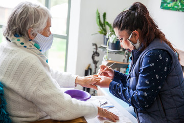 Senior woman getting a manicure at home during Covid-19 pandemic wearing face mask