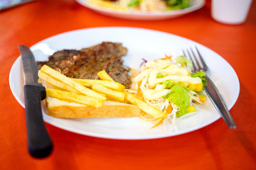 Dish of beef steak with salad, french fries and bread on red background