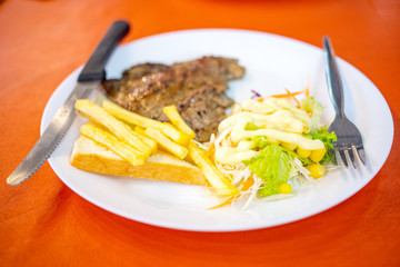 Dish of beef steak with salad, french fries and bread on red background