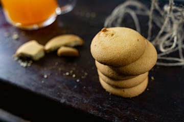 Fototapeta na wymiar Homemade shortbread, round-shaped pastry on a dark old surface in a stack of crumbs. Next to it is a glass mug with orange mulfruit juice